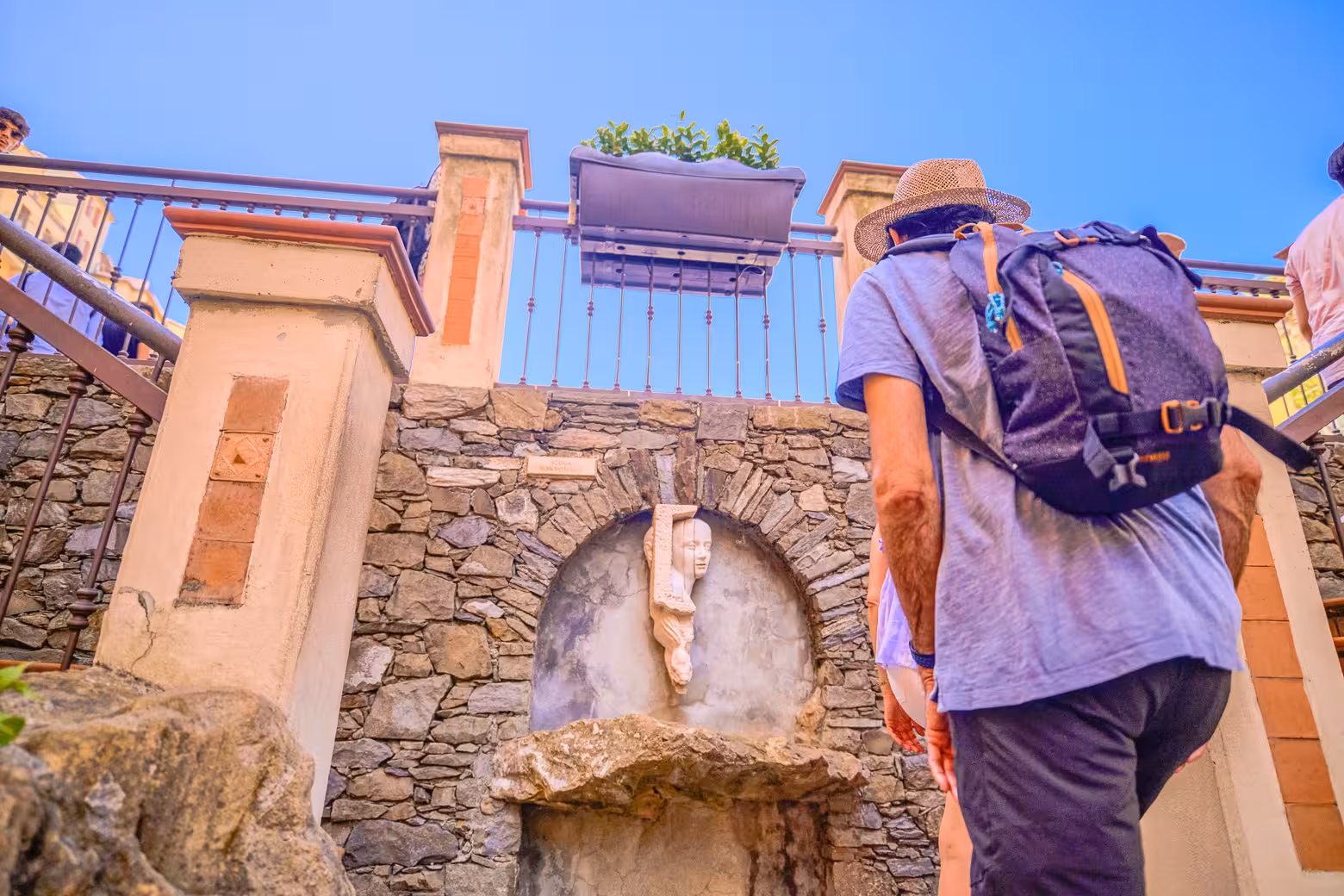 Traveler with backpack admires stone sculpture on scenic path in Cinque Terre, a highlight of the full-day tour from Florence.