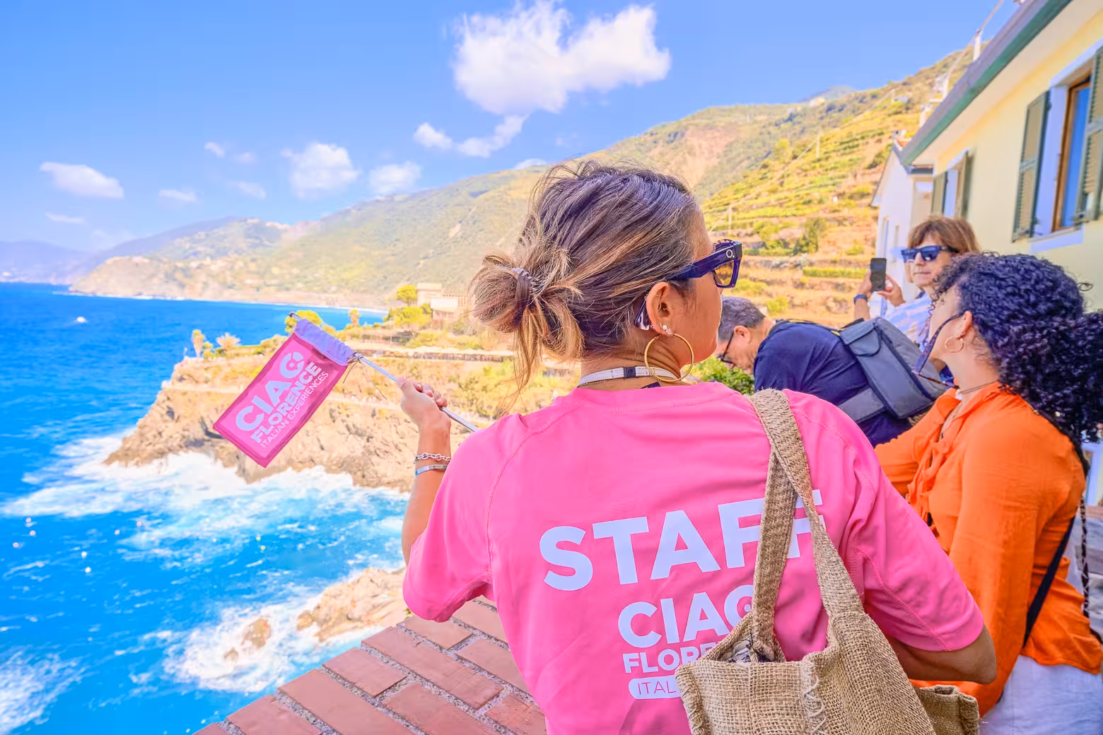 Tour guide in pink shirt leading a group with stunning views of Cinque Terre's rugged coastline.