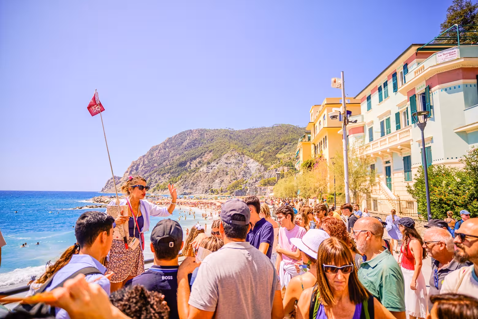 Tour guide leading a group near the beach in Monterosso, Cinque Terre, with vibrant buildings and sea view.