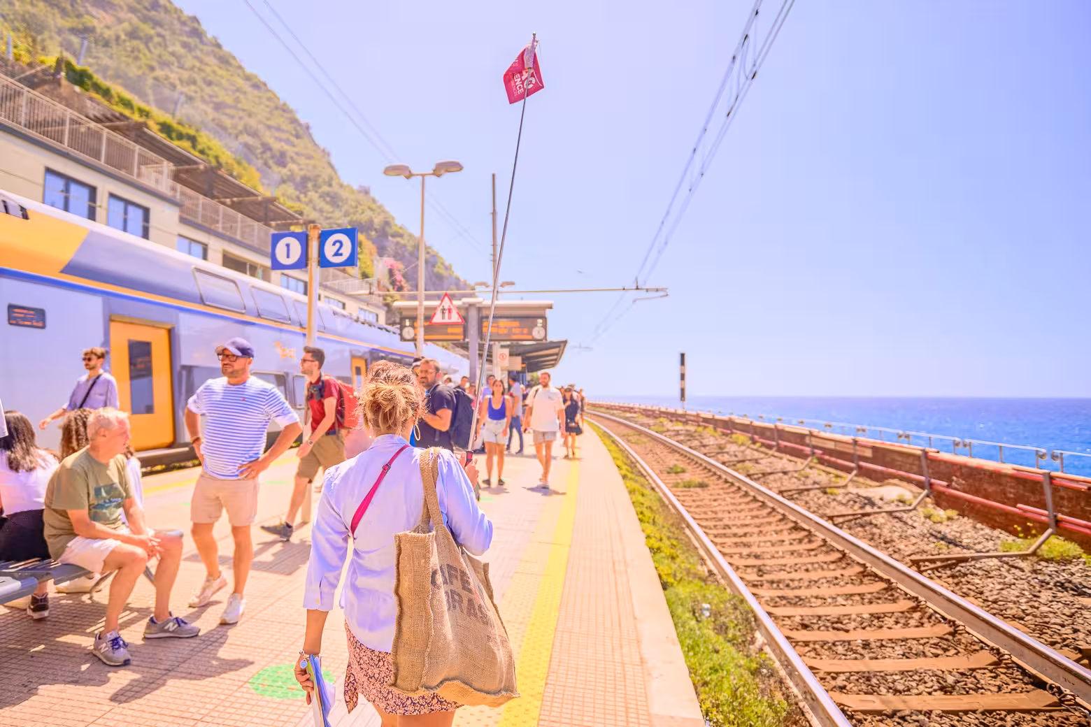 Tourists at a Cinque Terre train station platform overlooking the sea during a full-day tour from Florence.