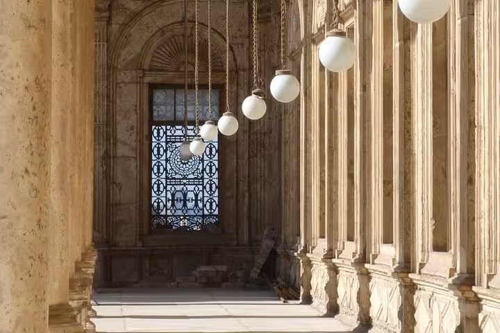 Historic corridor with hanging globe lights and carved stone columns at the Citadel, Cairo museum tour scene