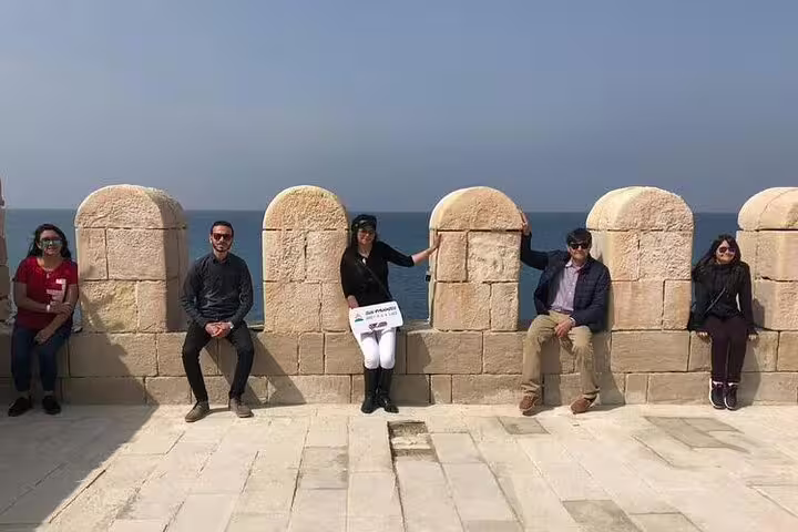Travelers relax on Citadel of Qaitbay sea wall, scenic stop on private Alexandria shore excursion tour