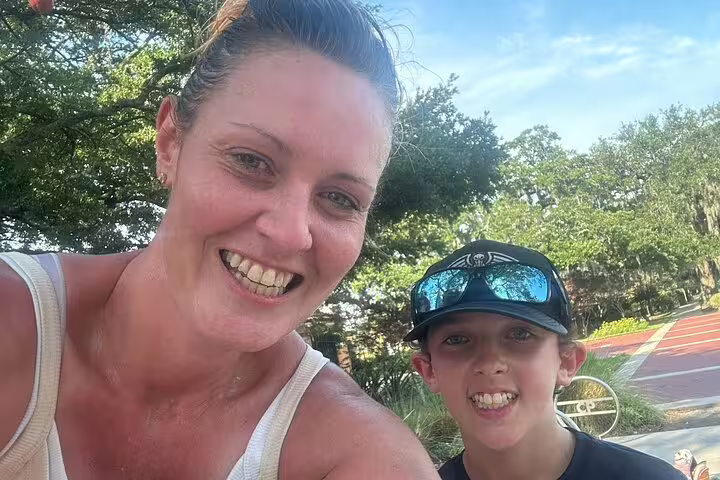 Smiling woman and young boy taking a selfie outdoors near a park track on a sunny day