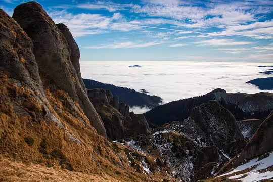 Rocky mountain peaks of Ciucas rising above a sea of clouds with snow patches in Romania
