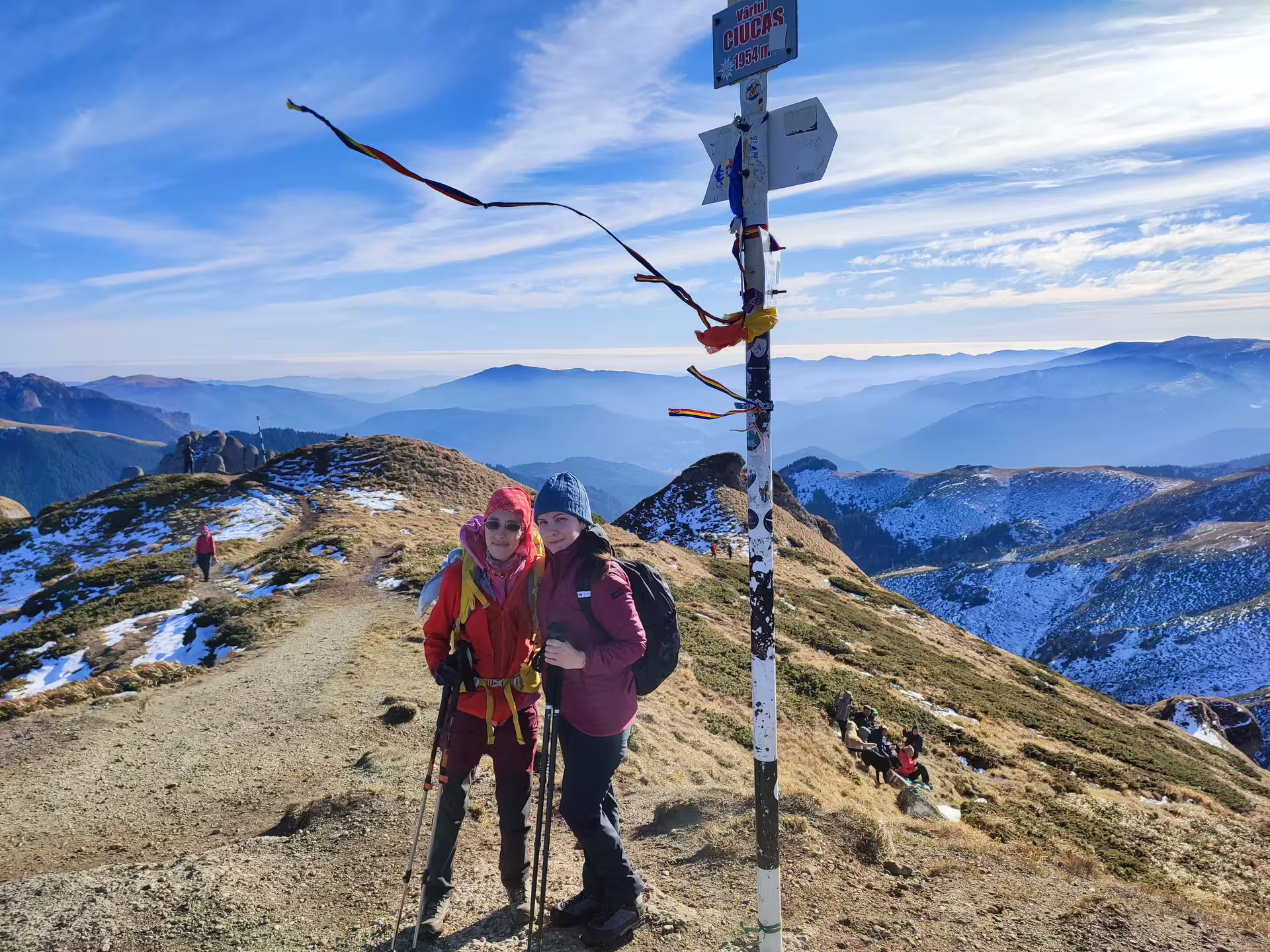 Two hikers at Vârful Ciucas summit marker 1954m with panoramic Romanian mountain views