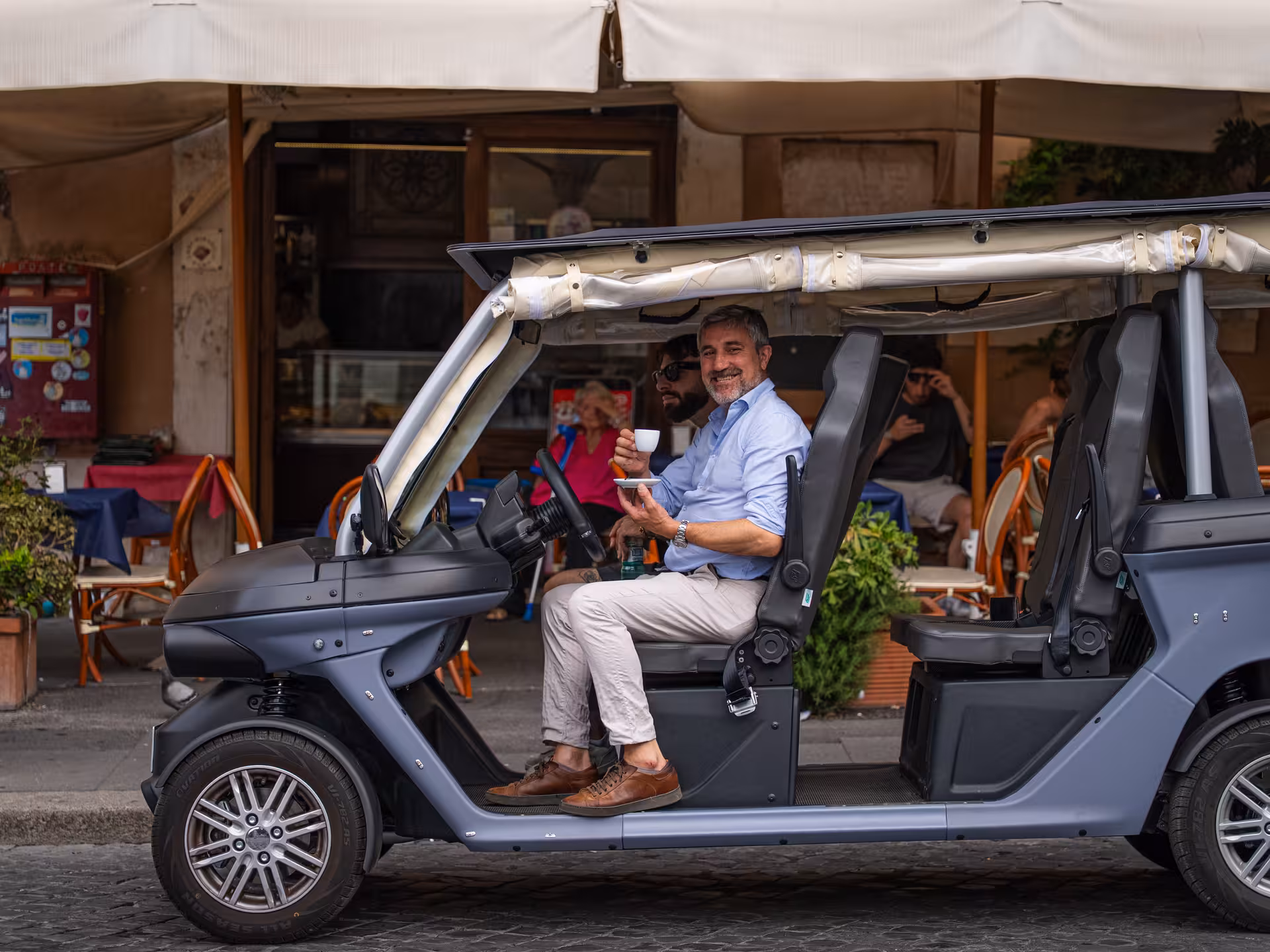 Smiling guide holding coffee in an open electric golf cart in central Rome on a Civitavecchia to Colosseum VIP transfer