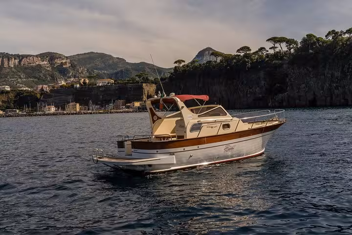Classic Gozzo 850 boat anchored off the scenic coastline of Sorrento with lush hills in the background.