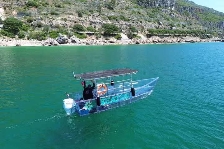 Transparent boat cruising in clear waters near Sesimbra's scenic coastline.