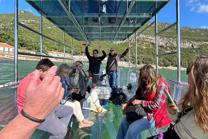 Tourists enjoying a scenic ride on a clear boat with views of Sesimbra's lush landscapes.
