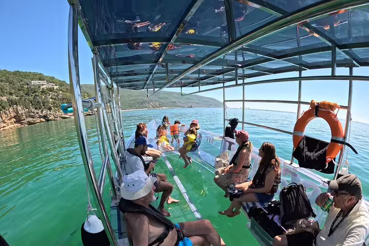 Tourists enjoying a scenic clear boat experience on turquoise waters departing from Sesimbra, Portugal.