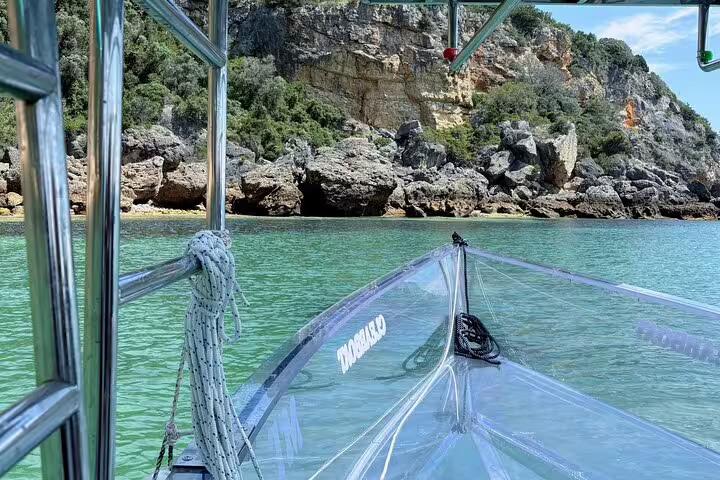 Clear boat navigating the serene turquoise waters near rocky cliffs on a Sesimbra adventure.