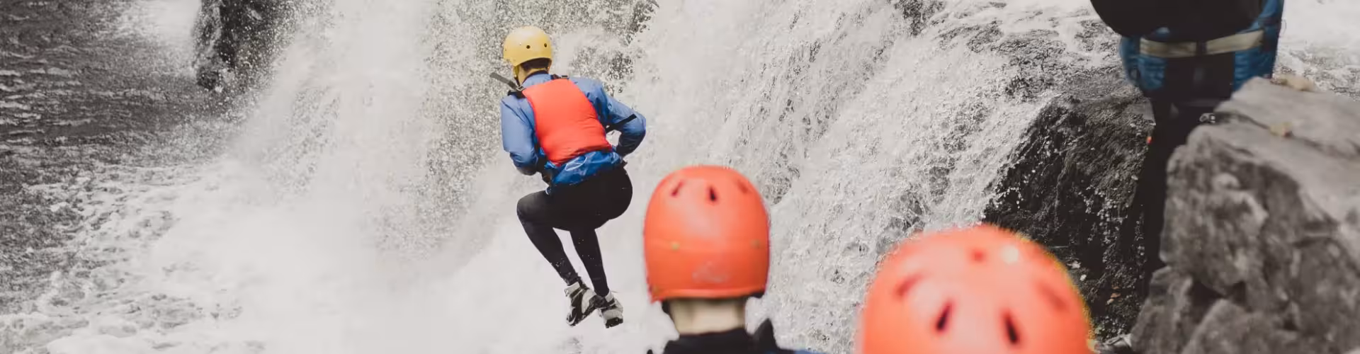 A group of adventure seekers wearing helmets and life jackets jumping into powerful crashing waves during an exhilarating coasteering experience.