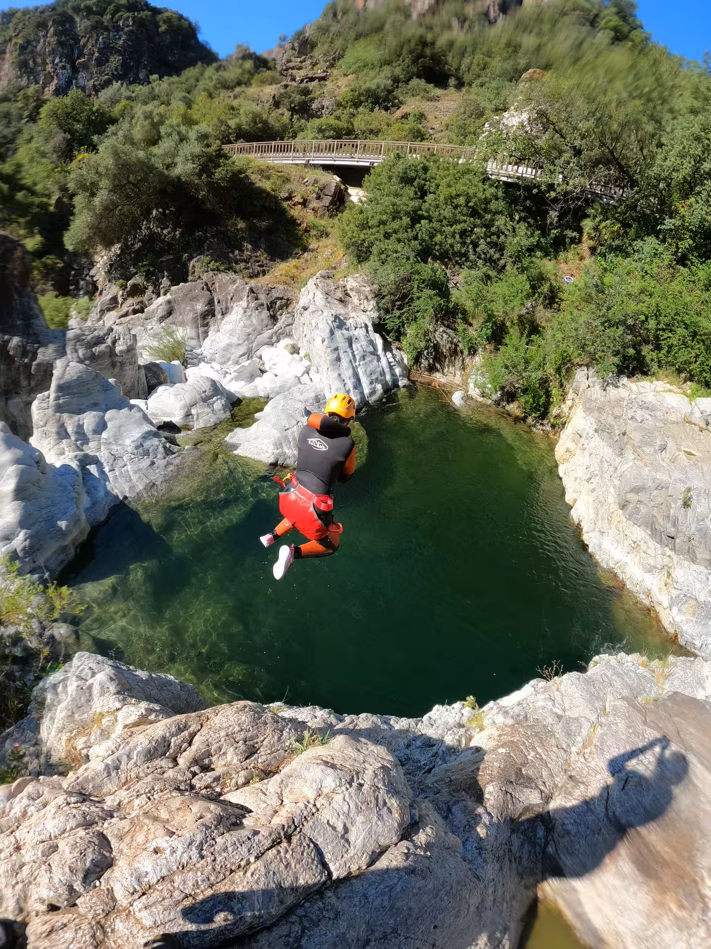 Adventurer in wetsuit and helmet cliff jumping into emerald pool during guided canyoning tour Guadalmina Canyon Estepona