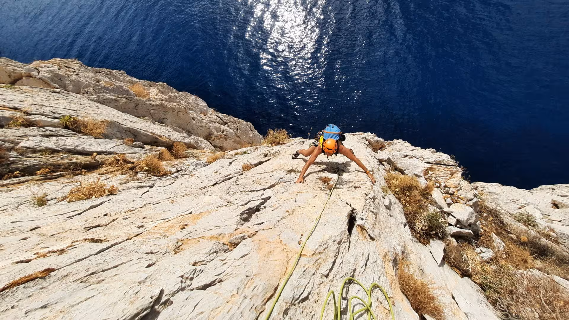 Climber scaling steep rock face above deep blue sea on Pan di Zucchero tour from Masua.
