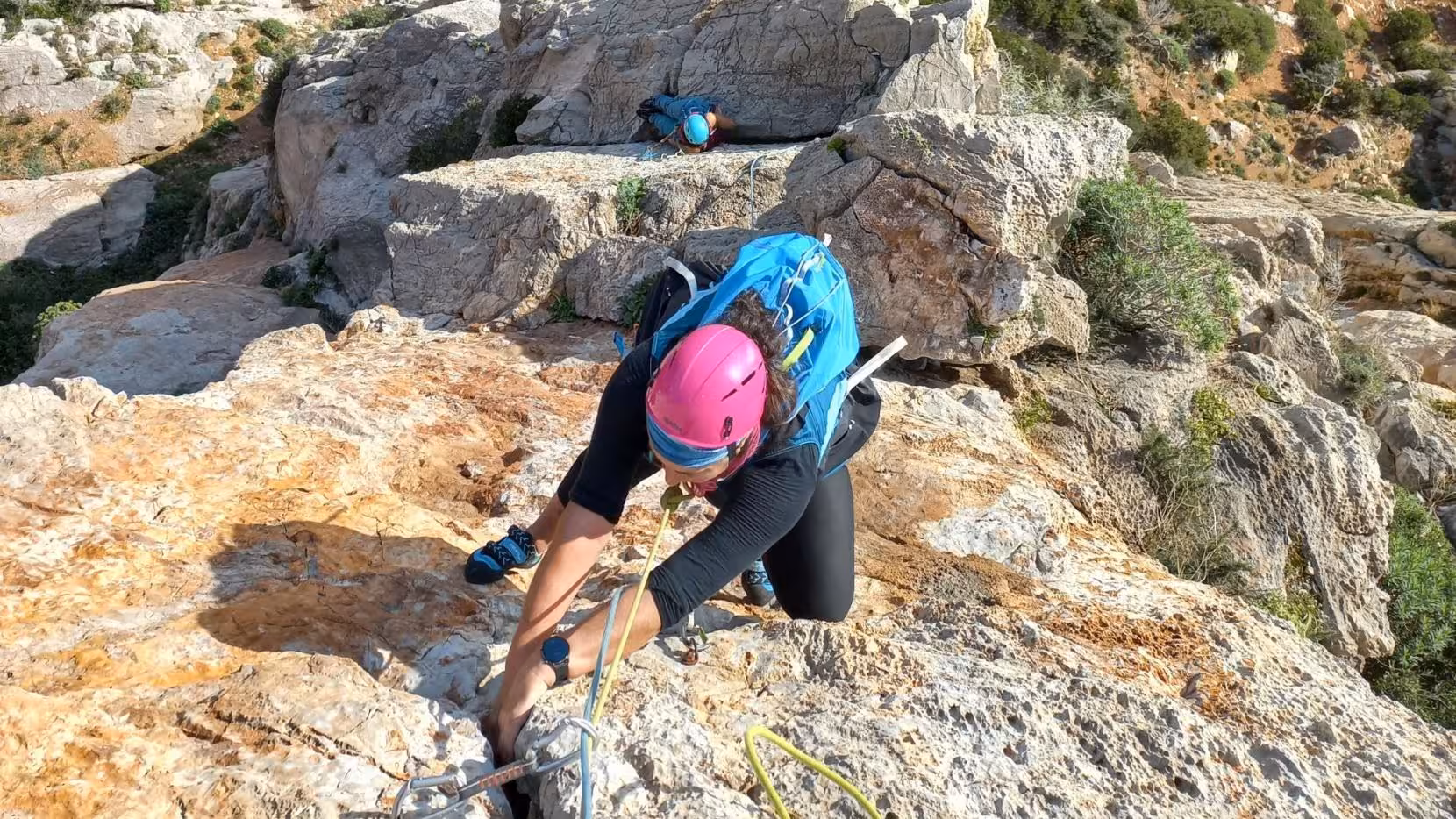Climber with pink helmet tackling rocky terrain of Masua, highlighting the thrilling Sardinian cliff experience.
