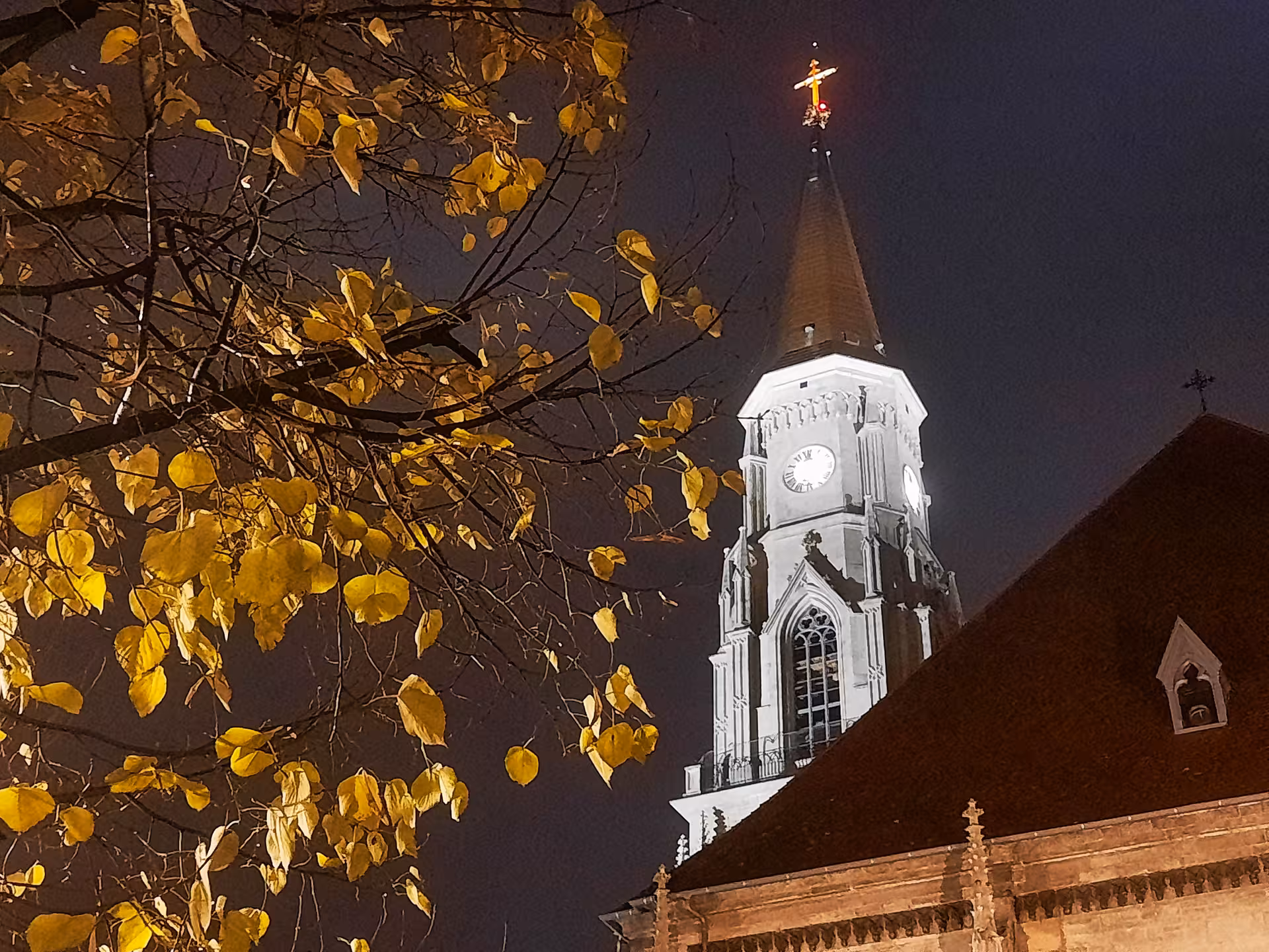 Illuminated historic church tower with clock and golden cross at night on Cluj guided walking tour