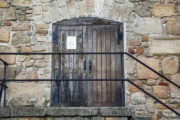 Ancient weathered wooden door set in stone wall of historic Cluj-Napoca building with iron railings