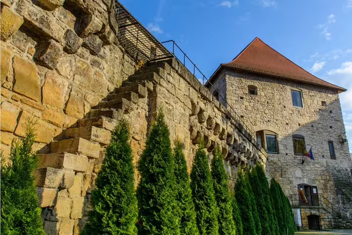 Medieval stone fortress wall with cypress trees and tower in Cluj-Napoca historic city center