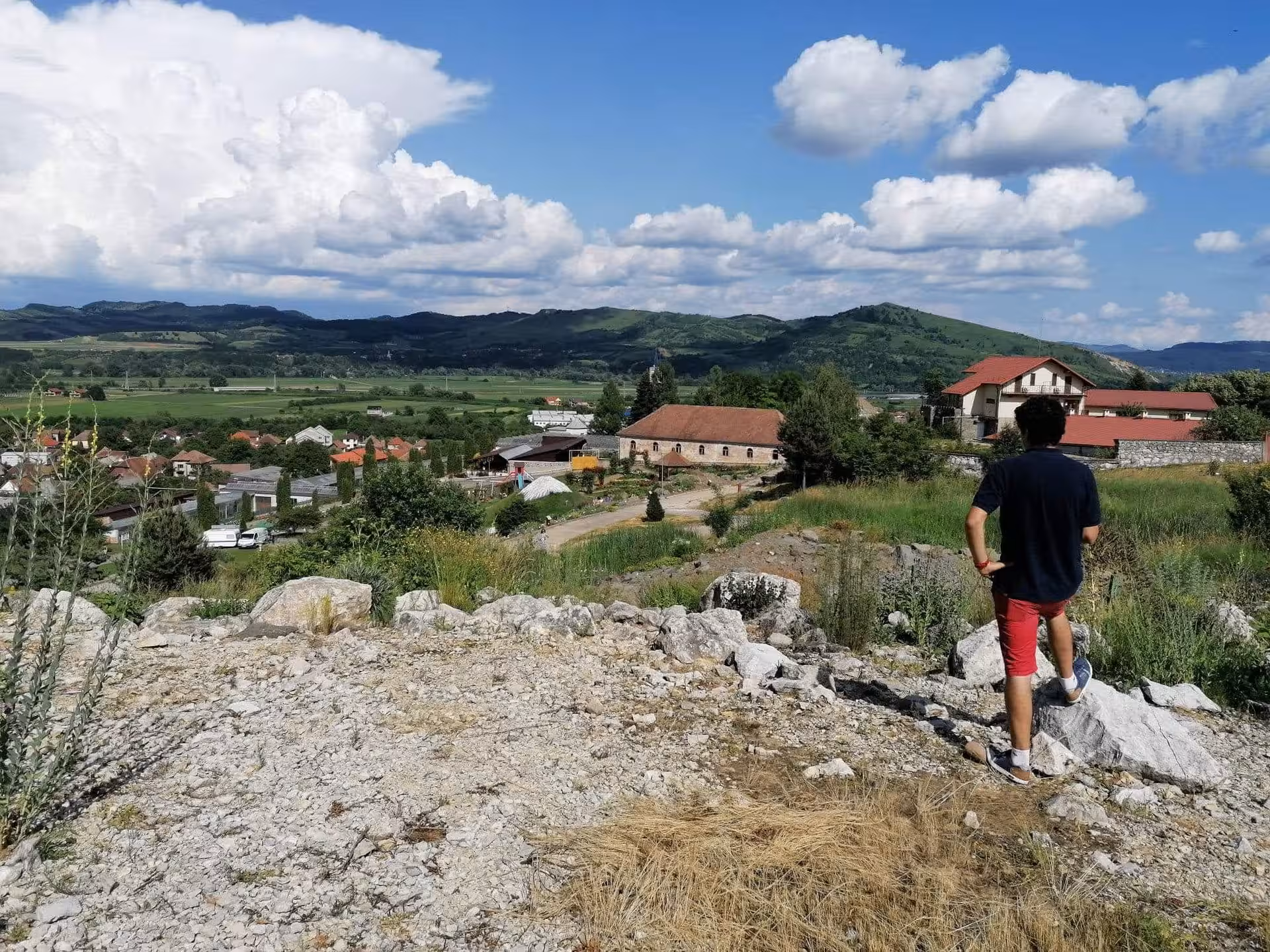 Person standing on rocky hilltop overlooking Salaj village valley with green mountains and blue sky