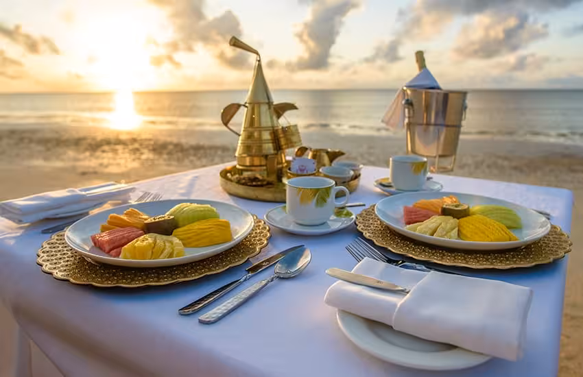 Elegant beachside breakfast setup with tropical fruits and coffee at sunrise during Coast Golf Adventure tour.