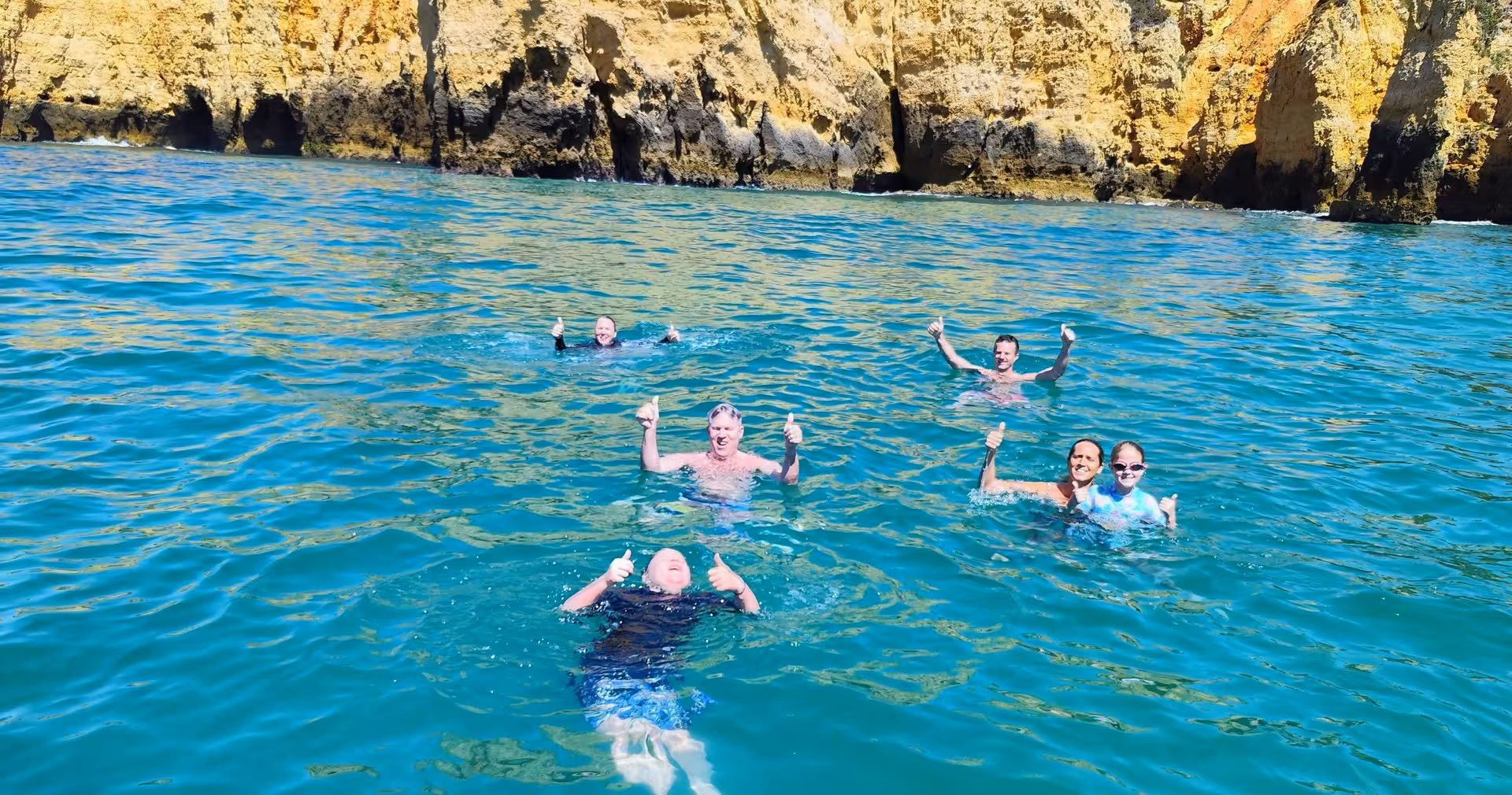 Happy group swimming in clear turquoise water beneath golden Ponta da Piedade cliffs on a Lagos coastal boat trip