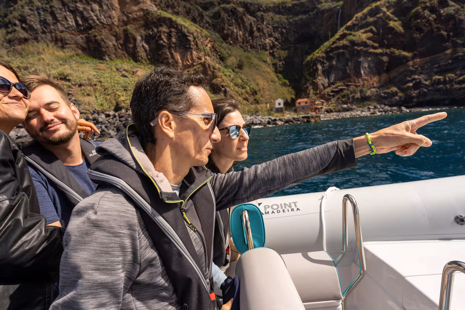 Tourists admire stunning coastal views on a RIB boat tour, with one pointing to a distant landmark.