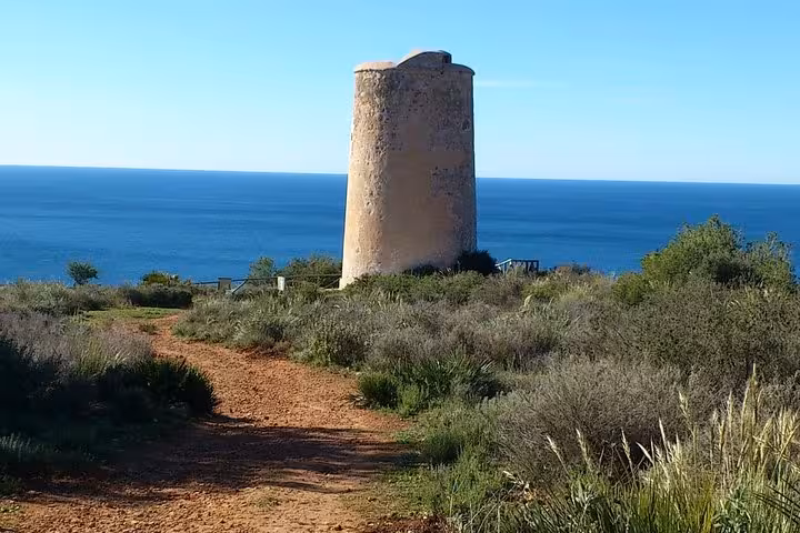 Historic stone tower surrounded by greenery on a scenic coastal trail near Malaga, offering panoramic ocean views.