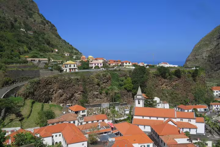 Scenic view of a coastal village with terracotta roofs nestled between lush green hills and a vibrant blue sea, perfect for a half-day jeep wine tour and tasting adventure.