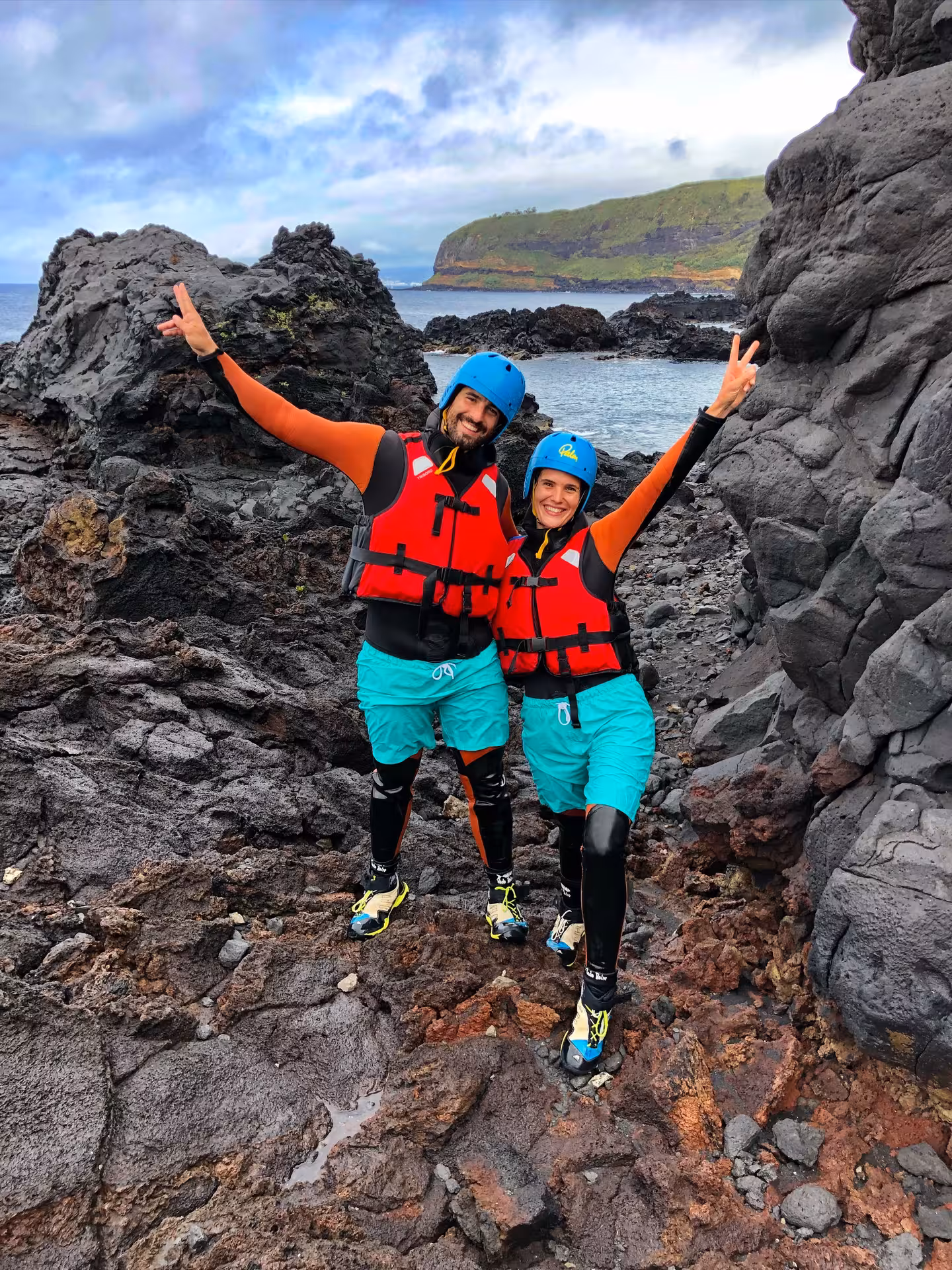 Smiling coasteering Freshman duo in helmets and buoyancy aids on volcanic coastline, ready to explore