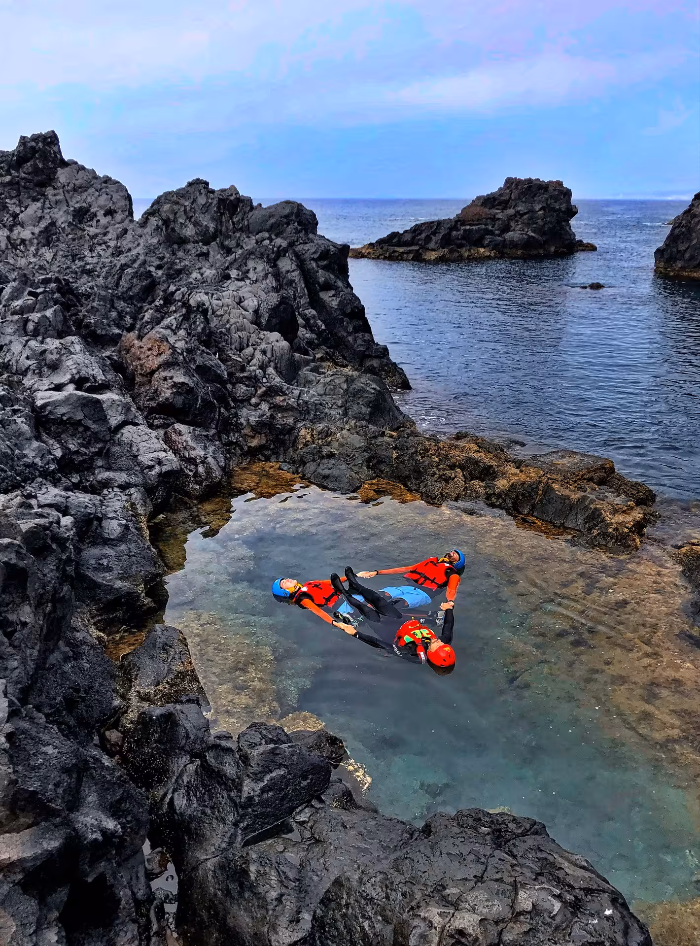 Coasteering Freshman participants floating in a rocky tidal pool in wetsuits, helmets and life vests