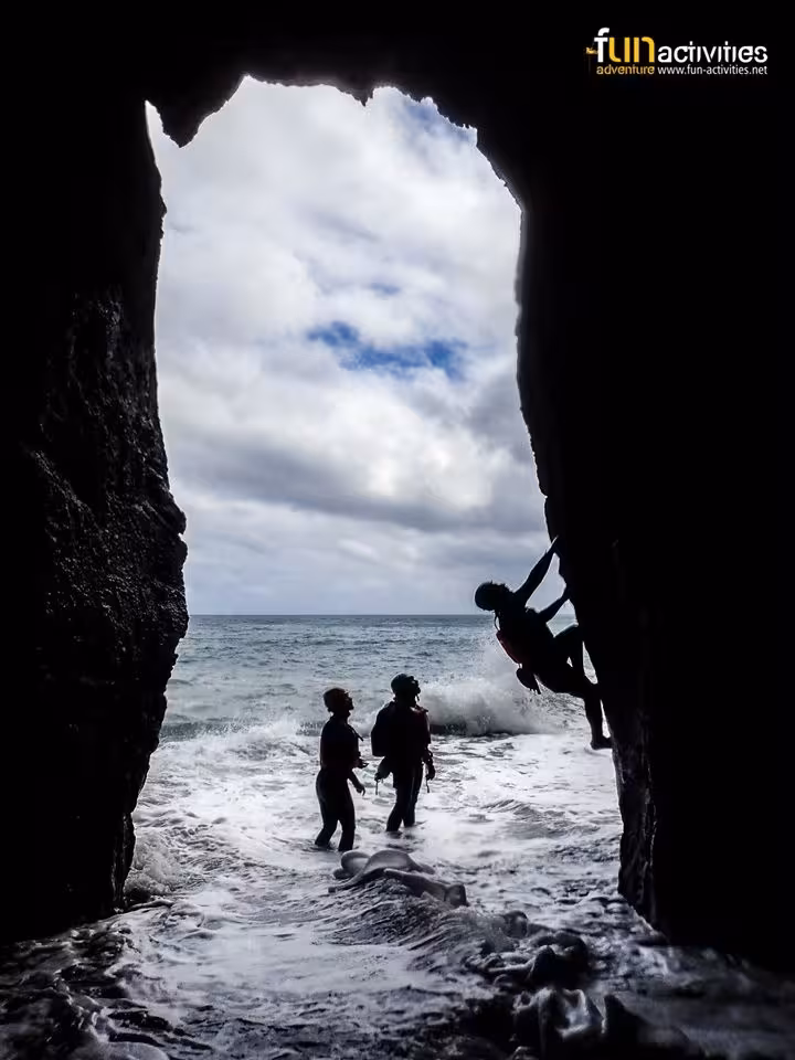 Coasteering Freshman sea cave exit with climber on rock wall and waves below, guided coastal adventure