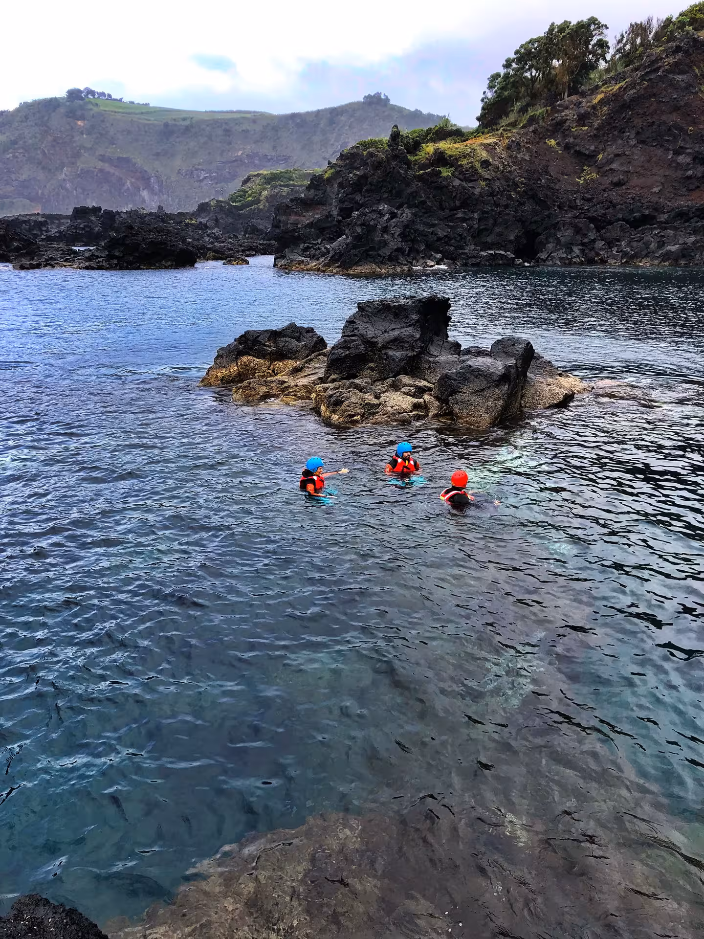 Coasteering Freshman tour group floating in clear sea beside rugged volcanic rocks on a scenic coastline