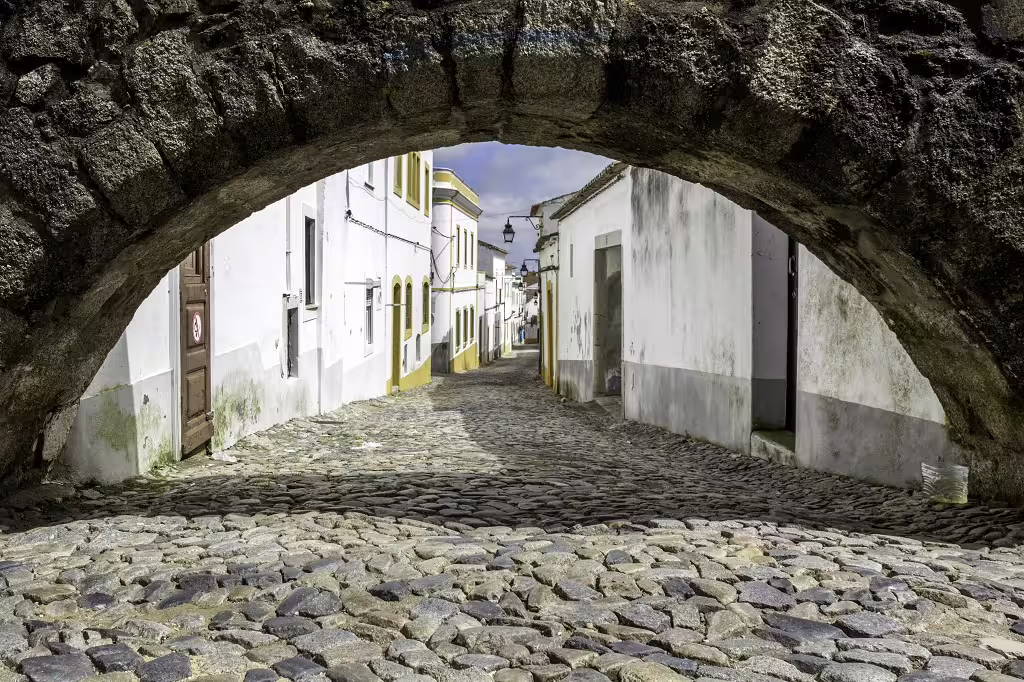Charming cobblestone street under ancient stone archway in a picturesque village in southern Portugal near Lisbon.