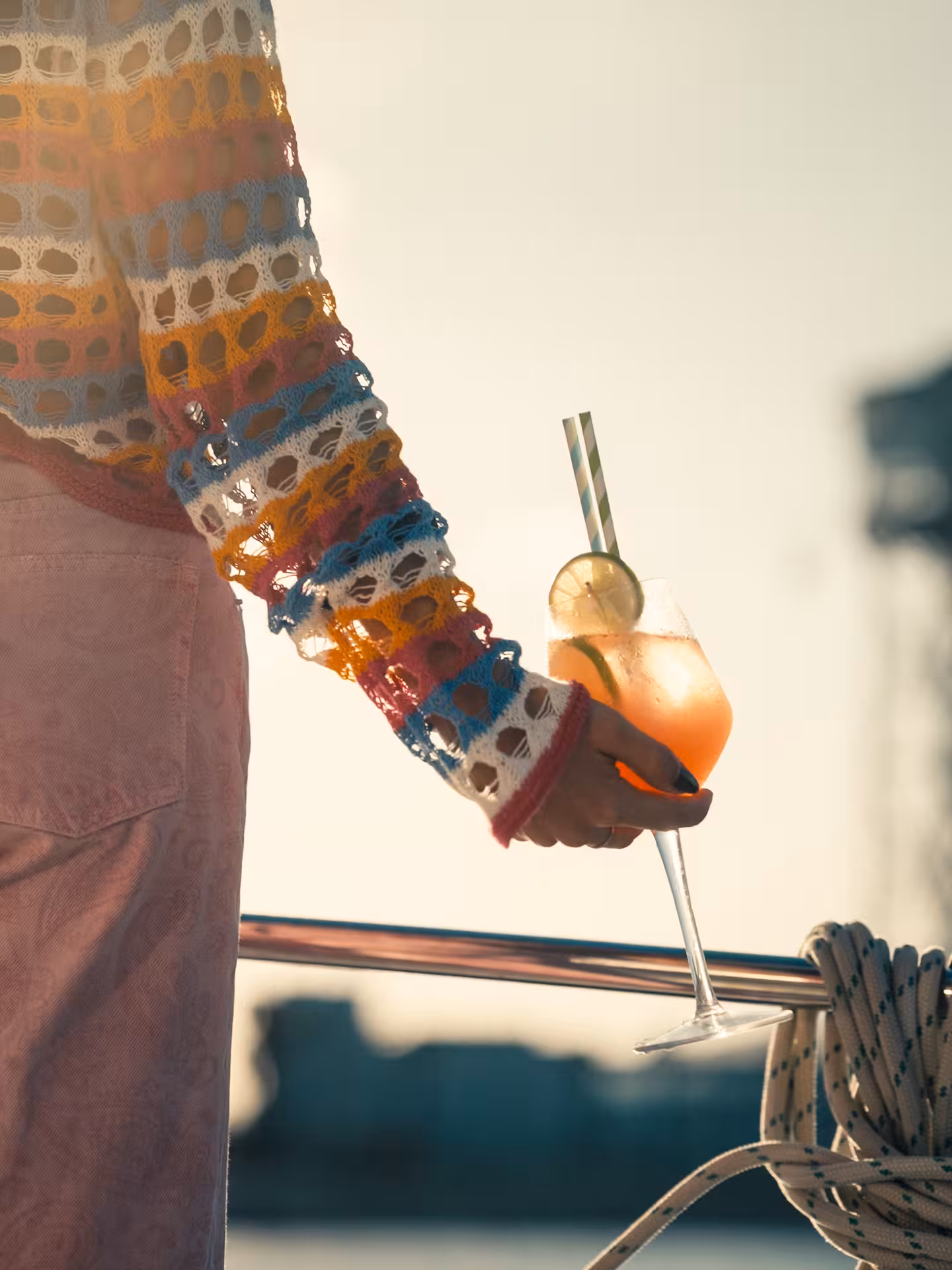 Hand holding a citrus cocktail with lime garnish on a yacht deck, perfect for a cocktail masterclass experience