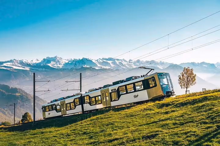 Cogwheel train rides through the Swiss Alps with snow-capped peaks in the background, offering breathtaking scenic views.