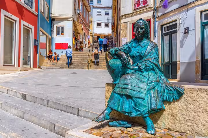 Bronze statue of a woman with a jug in a picturesque alley of Coimbra, showcasing vibrant architecture and local culture.