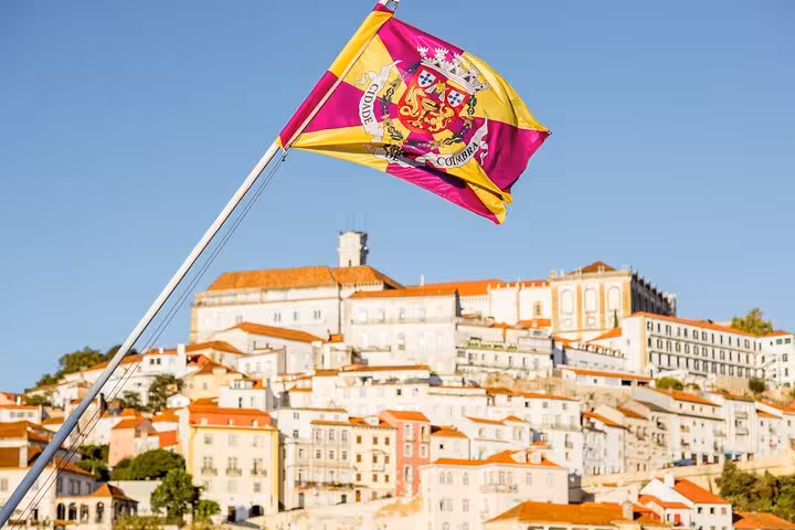 Discover Coimbra's vibrant cultural heritage as a colorful flag waves over iconic hillside architecture on an intro city walk.