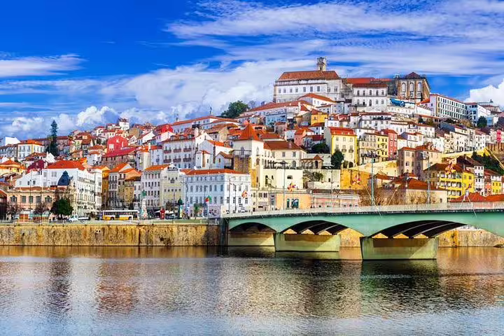Picturesque view of Coimbra's colorful hillside buildings with a serene river foreground, seen on the Porto tour.