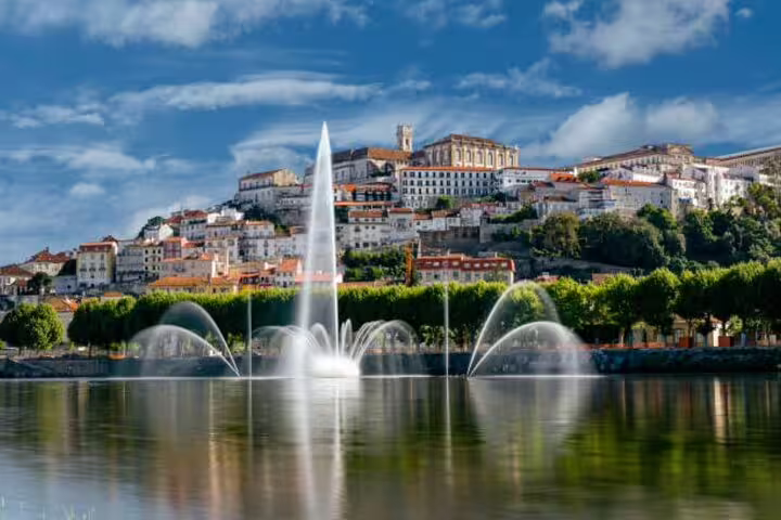 Scenic view of Coimbra with historical architecture and a vibrant fountain reflecting in the water, perfect for a Lisbon day tour.