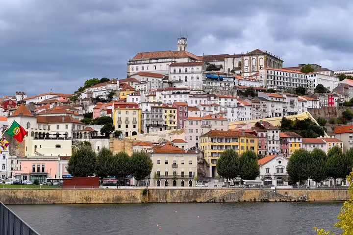 Scenic view of Coimbra’s historic hillside architecture beside the Mondego River, a highlight on the Porto to Lisbon private journey.