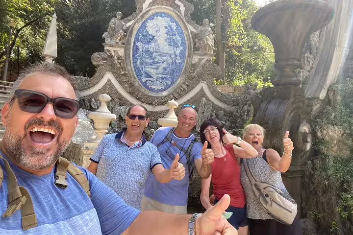 Happy travelers give thumbs up by Coimbra’s Quinta das Lágrimas azulejo fountain on a self-guided tour