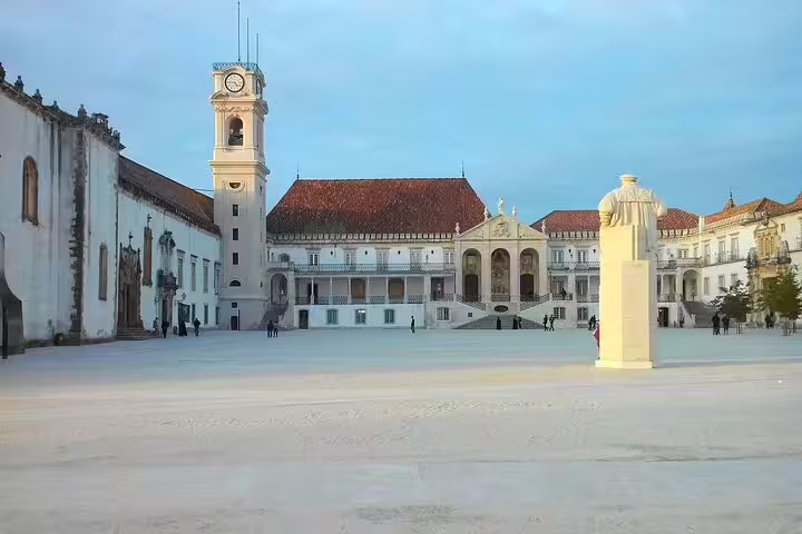 Historic University of Coimbra courtyard in Portugal, featuring grand architecture, a clock tower, and a prominent statue.