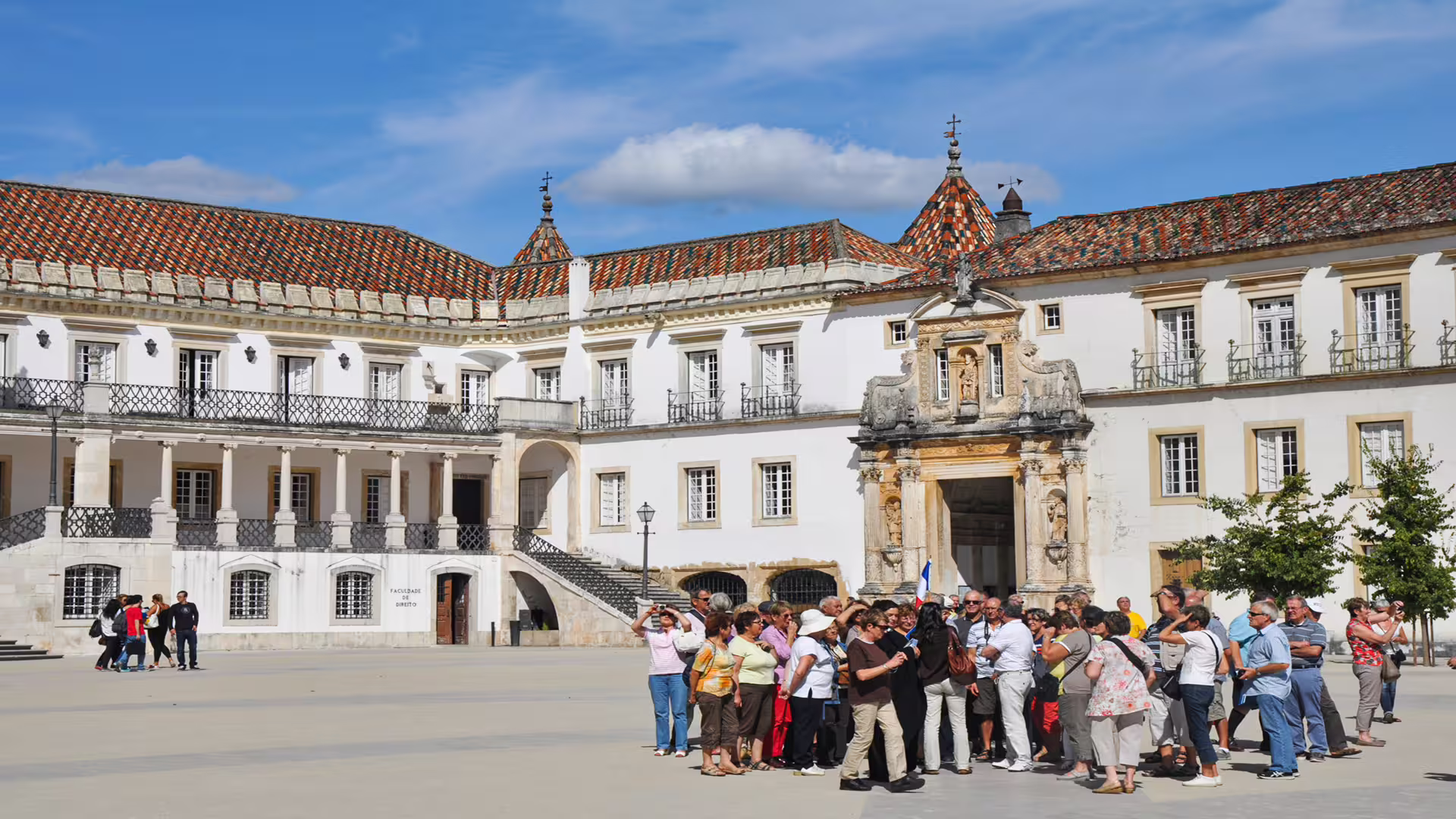 Group of tourists exploring the historic architecture of the University of Coimbra on a private guided tour under a clear blue sky.