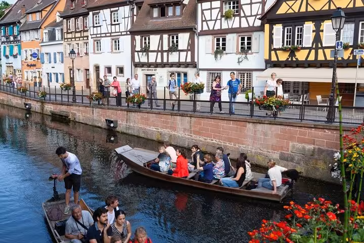 Tourists on a wooden boat tour along the canal in Colmar, France, with colorful half-timbered houses in background