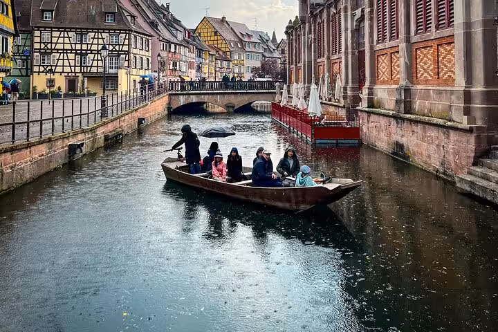 Tourists on a wooden boat tour through Colmar's historic canals with colorful half-timbered buildings