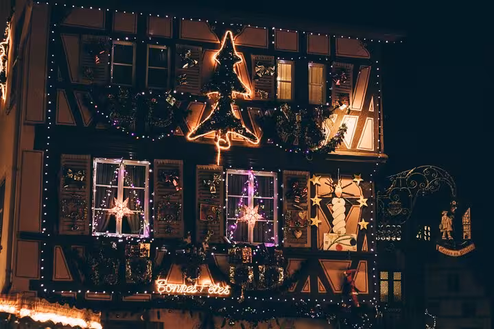 Colmar half-timbered building decorated with Christmas lights and Bonnes Fêtes neon sign at night