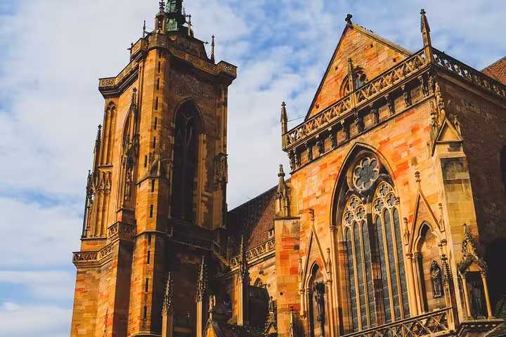 Gothic cathedral with ornate stone tower and stained glass windows in Colmar, Alsace