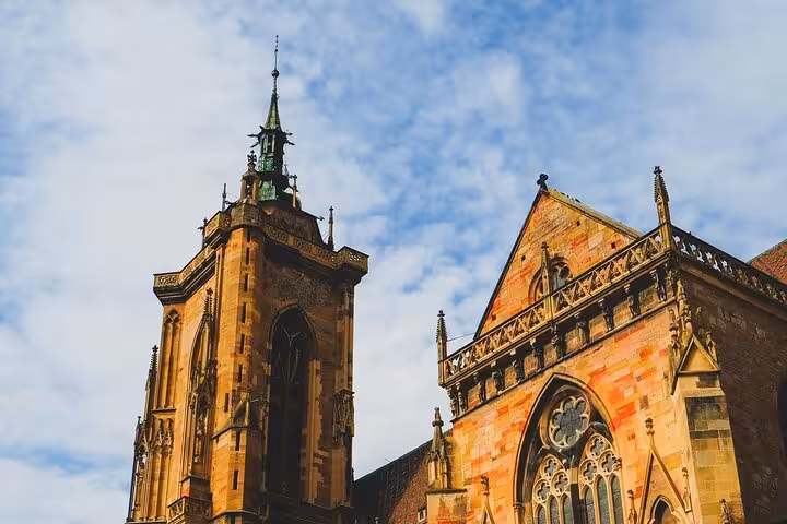 Gothic architecture of Colmar's historic church tower and facade under blue sky, Alsace France
