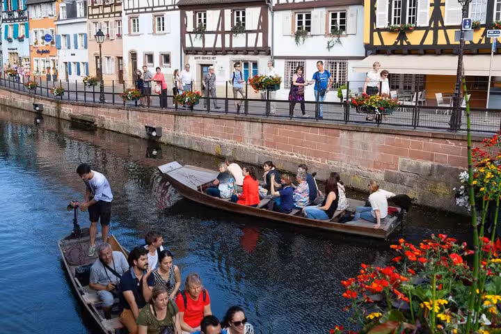 Tourists on wooden punt boats along flower-lined canal in Colmar's Little Venice, Alsace, France