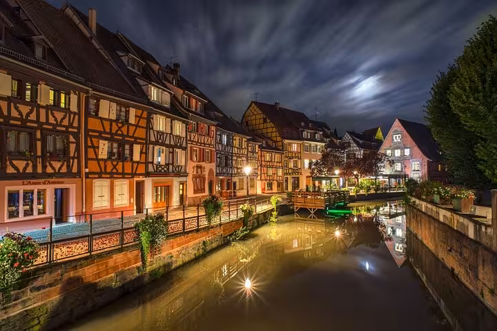 Colmar Little Venice canal at night with illuminated half-timbered houses reflecting in water, Alsace France